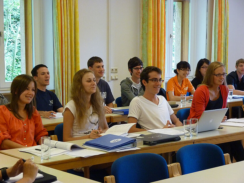 A group of students sitting in class, looking towards the front, and smiling. 