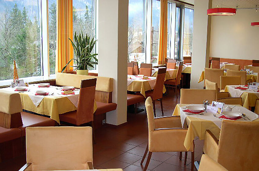 Dining hall with tables and chairs in warm colours with a big window front.