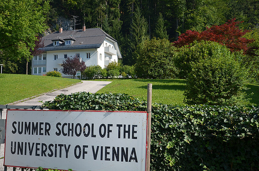 View of park area with one white three floor house in the Background and a sign reading 