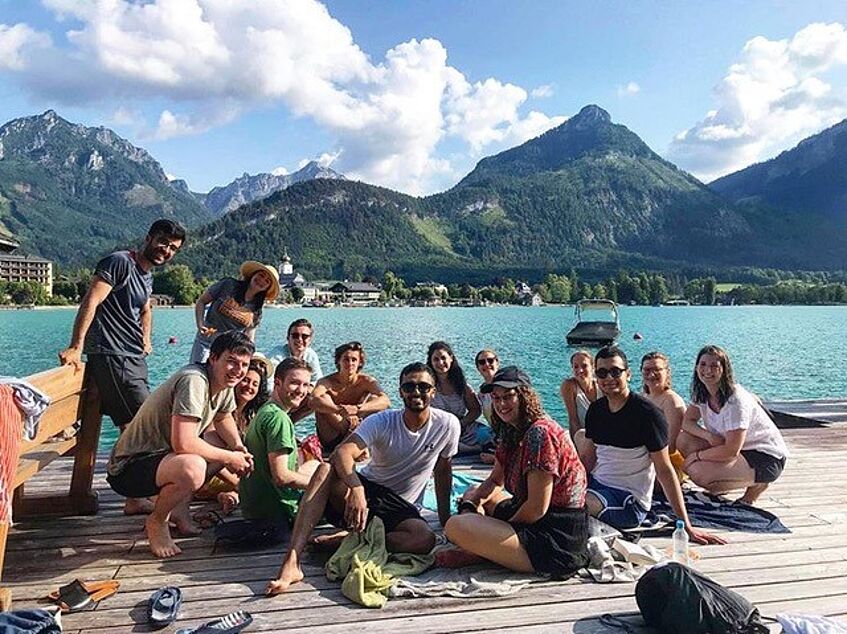 A group of young people on a pier with a lake and mountains in the background