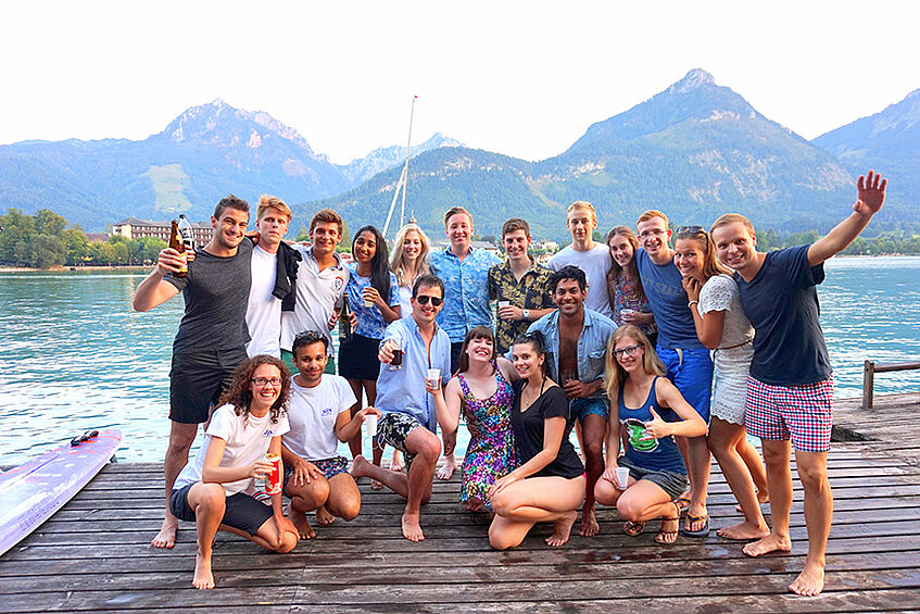 Group of cheering students on a wooden pier with lake and mountains in the background