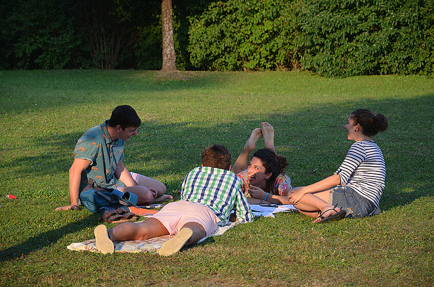 Four students sitting on the lawn, laughing.