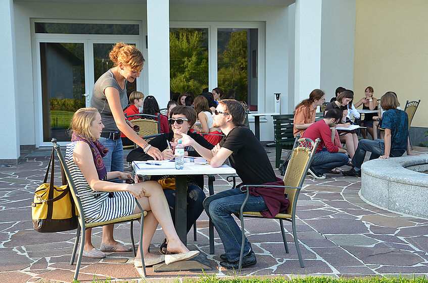 Three students sitting at a table on a terrace listening to the lecturer's demonstration. 