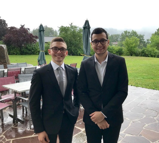 Two young men in suits in front of a lawn.